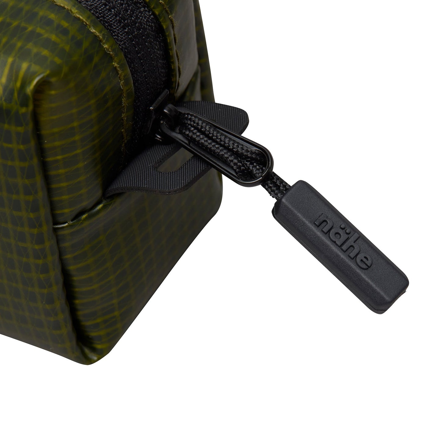 Close-up of the black zipper pull embossed with the Nähe logo on the Green grid-patterned pouch.