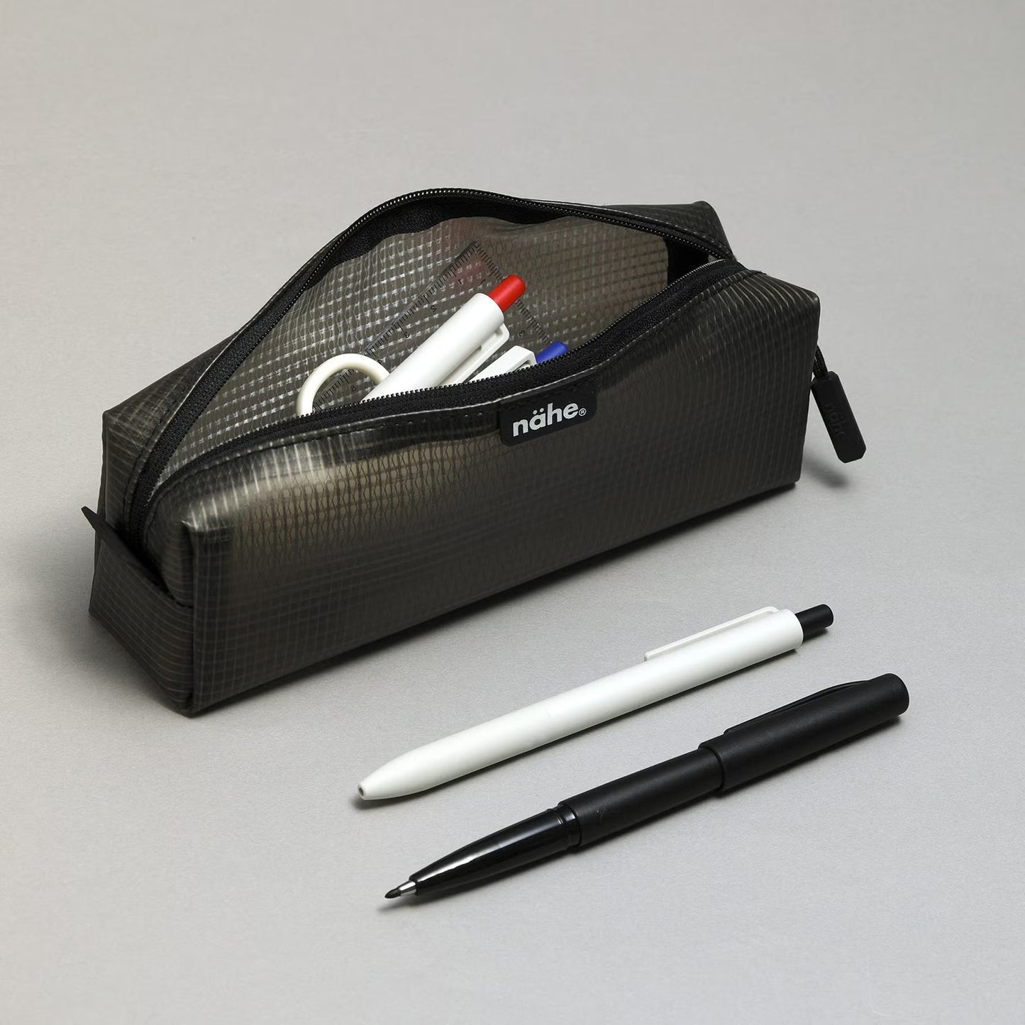 Nähe Soft Grid Pouch in Gray, unzipped and holding pens, with a white and a black pen resting beside it.
