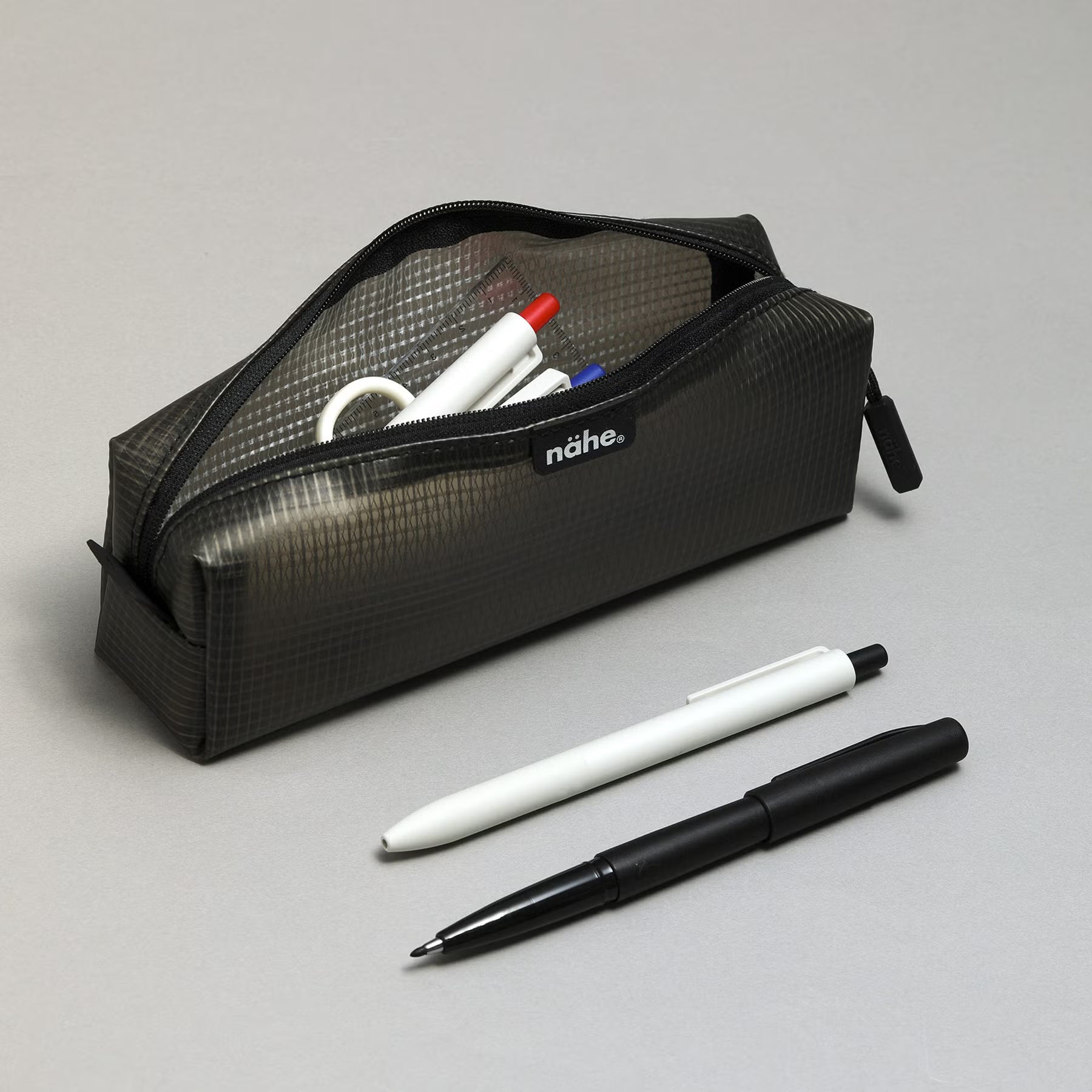 Nähe Soft Grid Pouch in Gray, unzipped and holding pens, with a white and a black pen resting beside it.